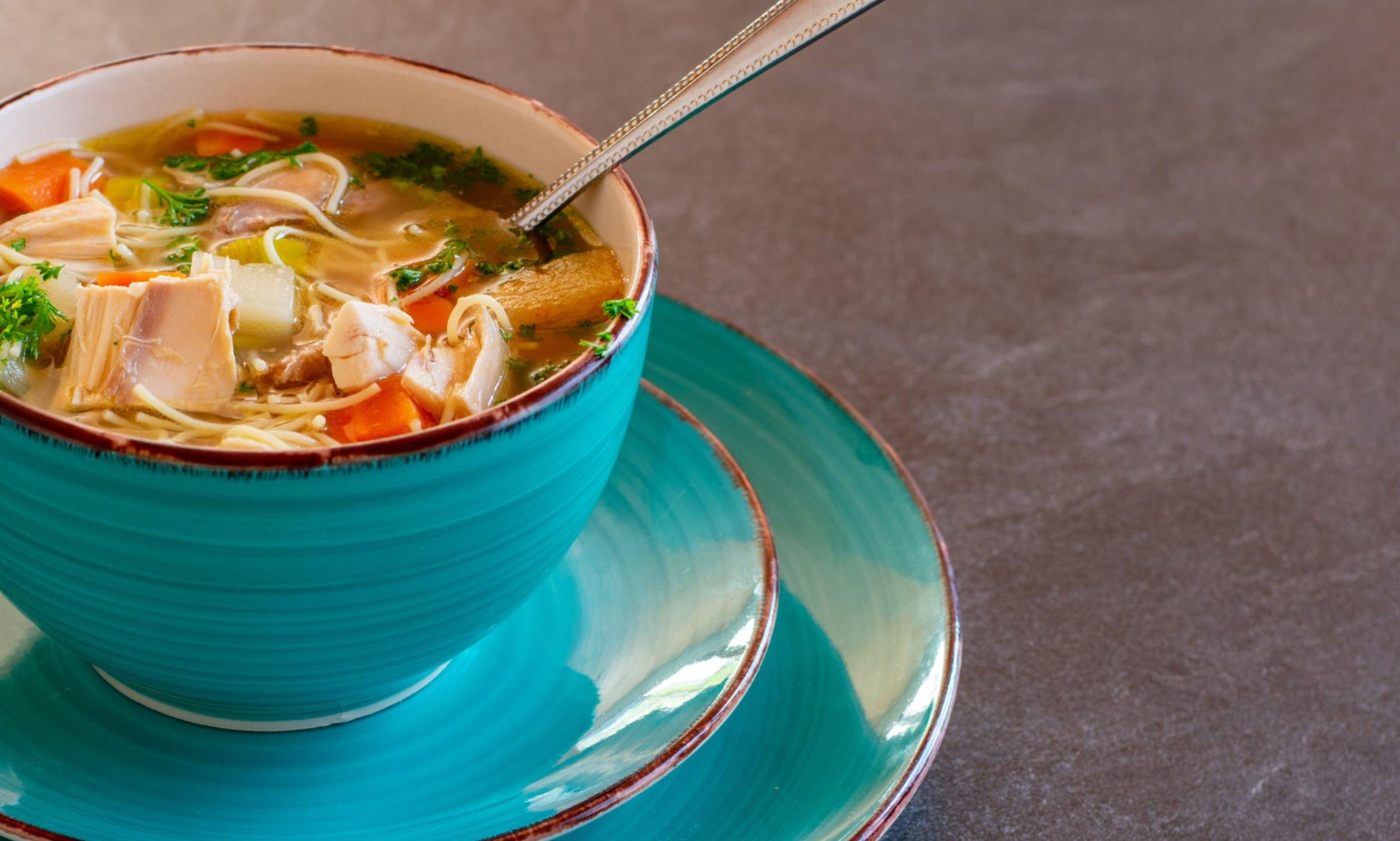 Warm bowl of chicken noodle soup served with golden-brown bread rolls on the side.